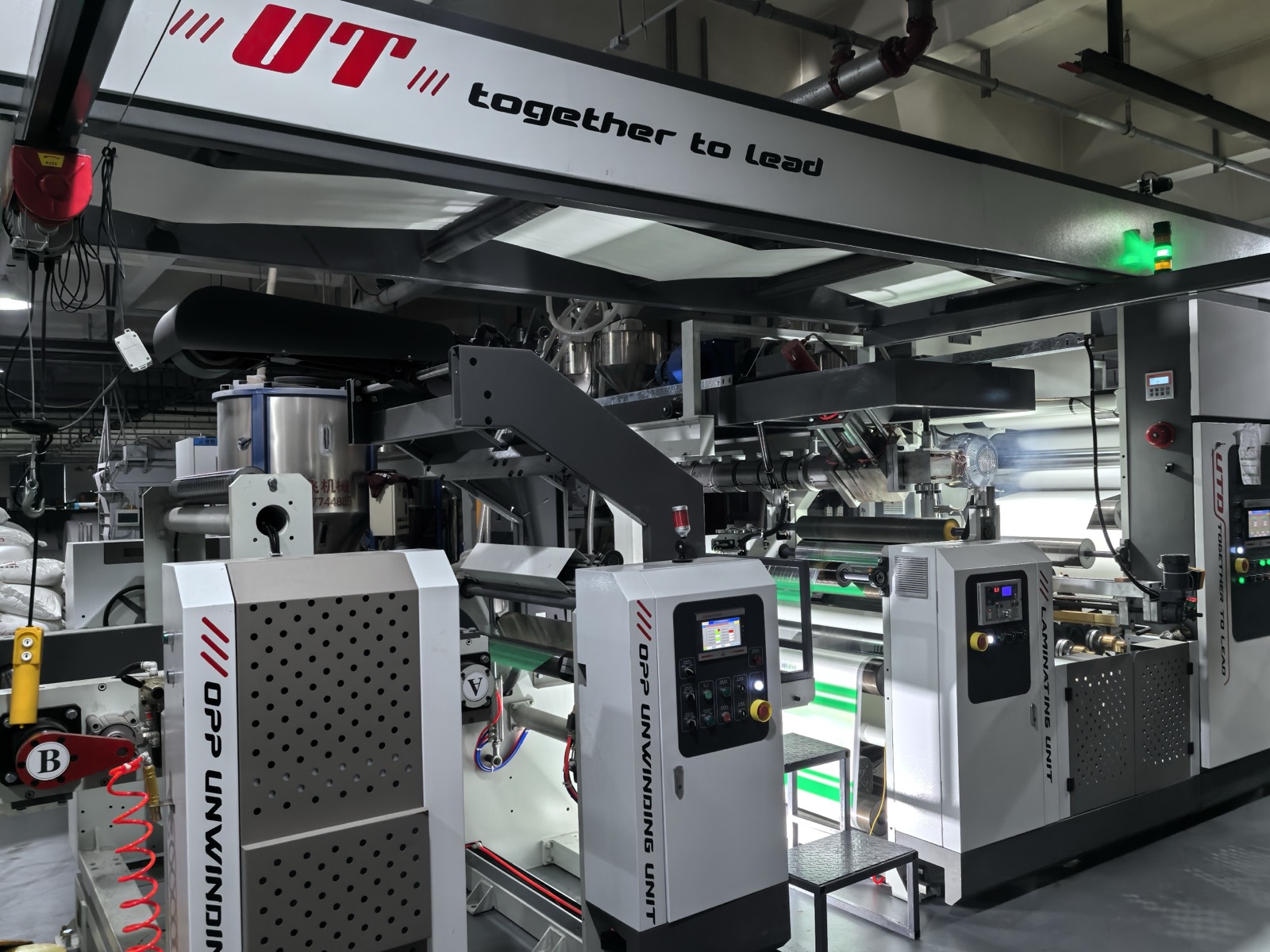 Extrusion coating line with film unwind stands and overhead resin hoppers