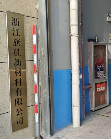 Brass company nameplate mounted beside a plant entrance, next to a fire-extinguisher cabinet and posted safety notices